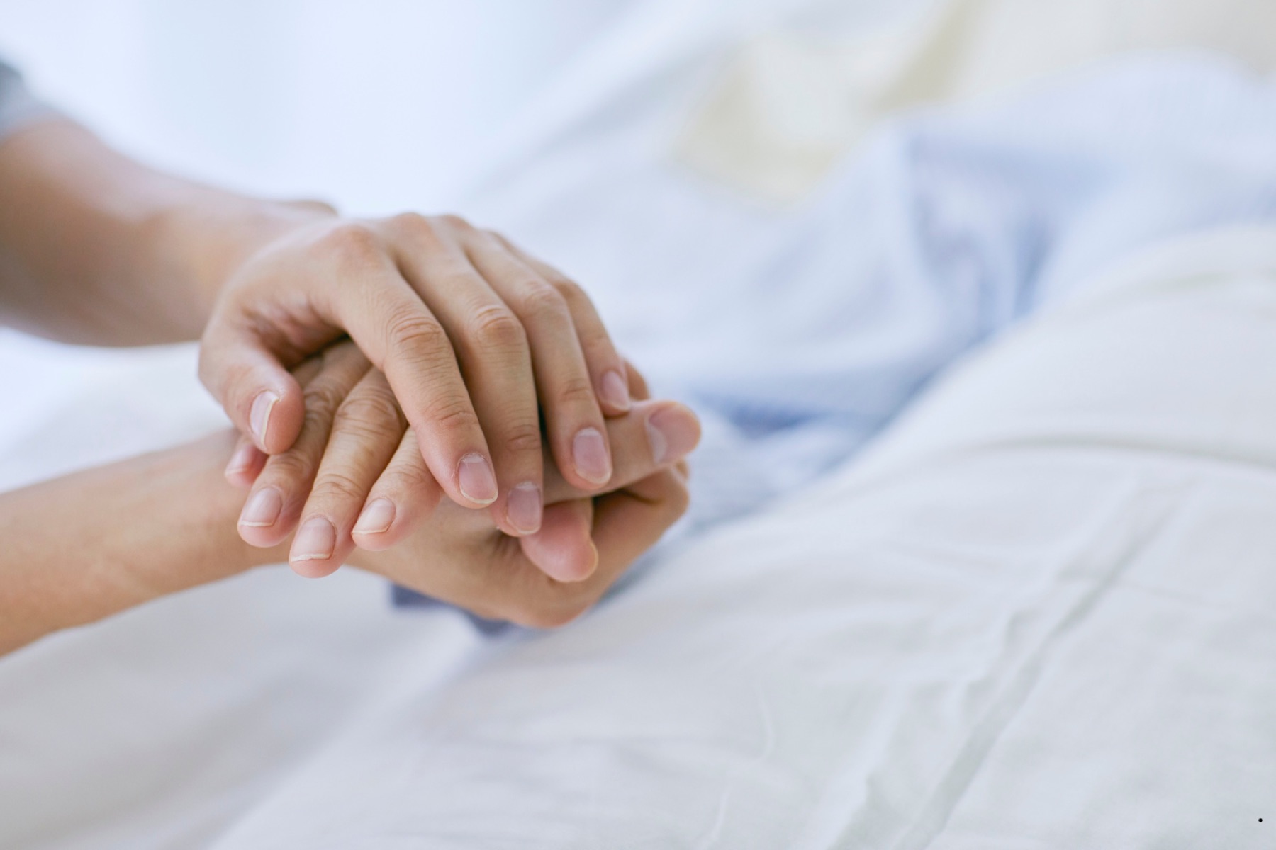 Pflegekraft hält bei der Pflege zu Hause behutsam die Hand einer Patientin